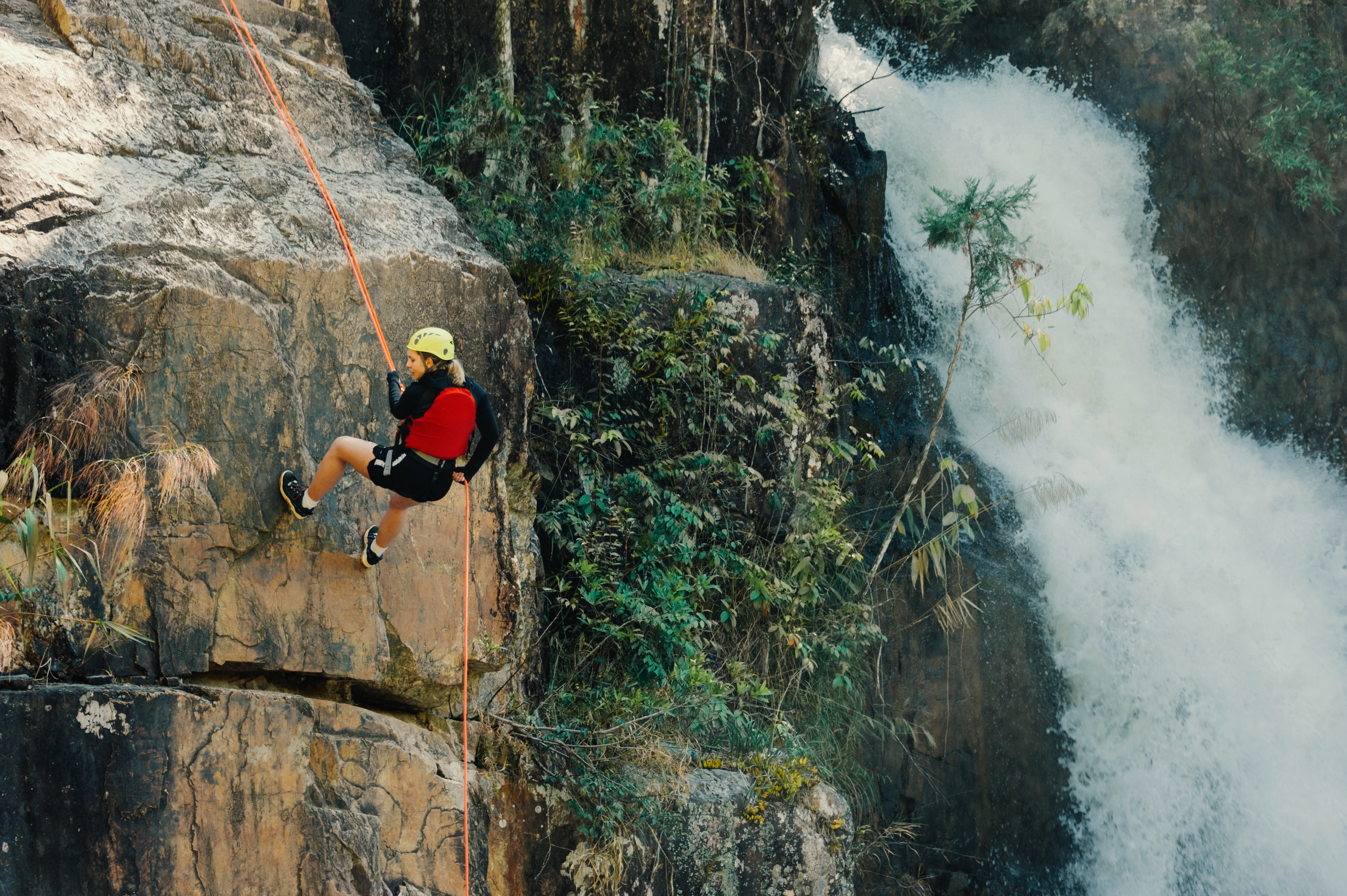 Man rockclimbing up a mountain with a waterfall next to him.